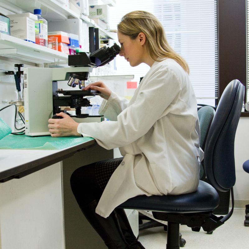 researcher in lab coat sitting at a microscope